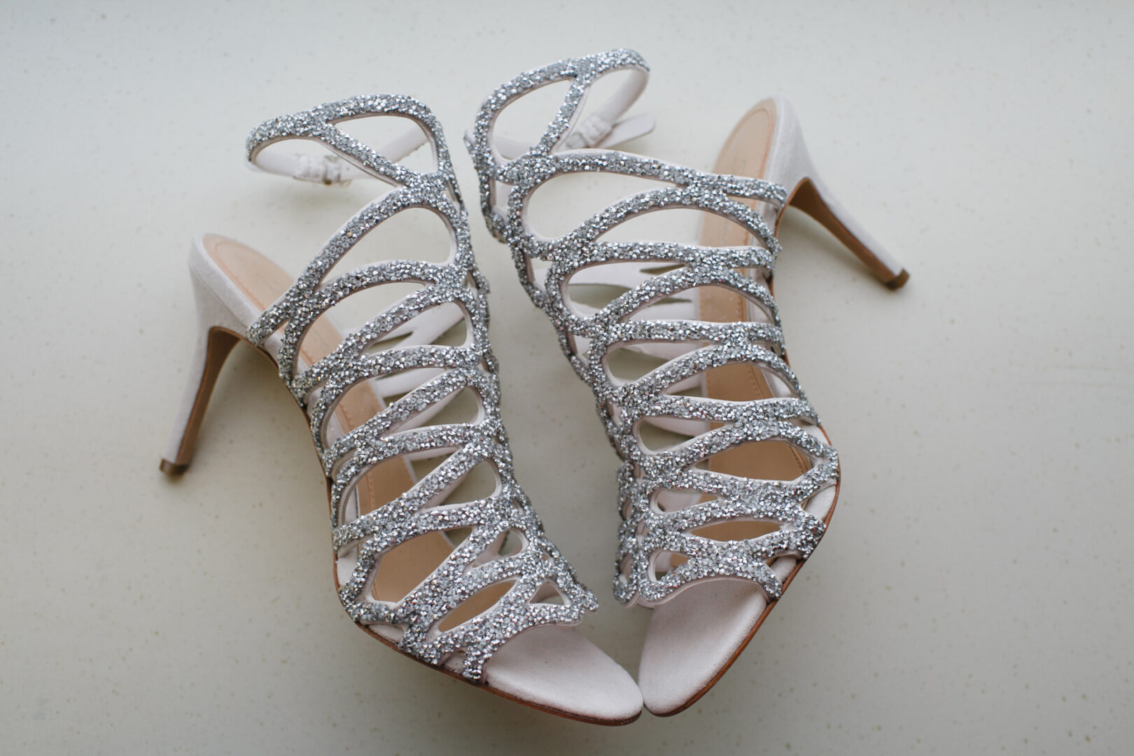 Sparkling with elegance, this pair of silver glittery high-heeled sandals features a chic strappy design, ideal for making a dazzling entrance at any wedding, especially one at the iconic Congress Hall in Cape May.