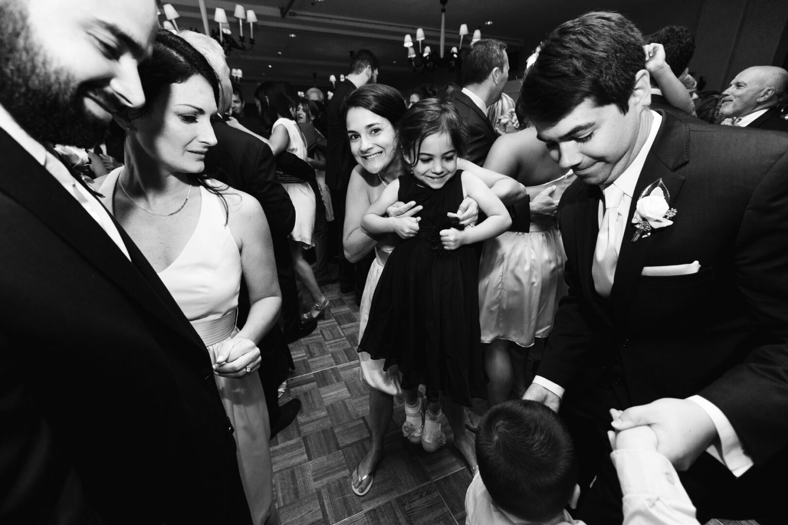 A black and white image captures a serene moment at Congress Hall, Cape May. A group gathers indoors; one woman cradles a child while others, dressed in formal attire, stand nearby, exuding an air of timeless elegance reminiscent of a classic wedding.