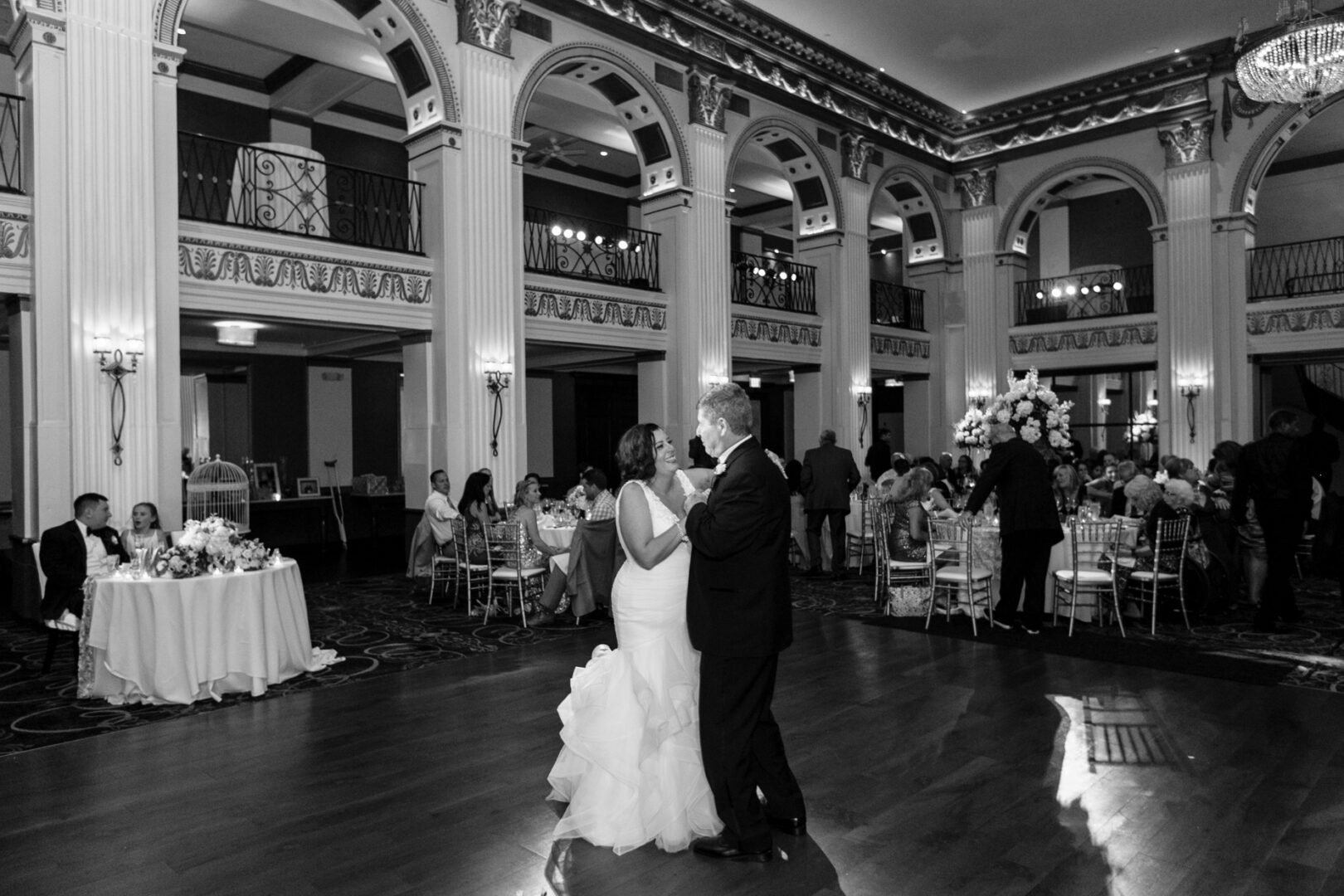 In the elegant Ballroom at the Ben, a couple in formal attire gracefully dances while guests enjoy the evening from their decorated tables.