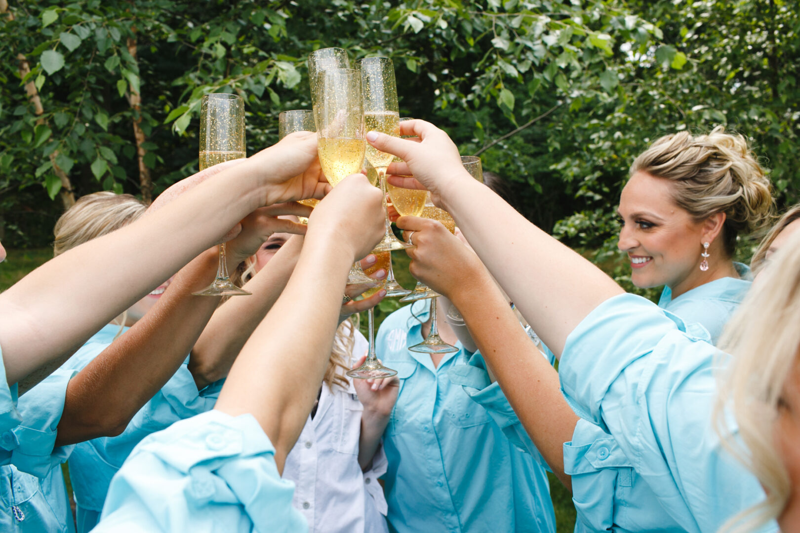 A group of people in light blue shirts joyously toasts with champagne glasses outdoors, celebrating as if at a Please Touch Museum wedding.