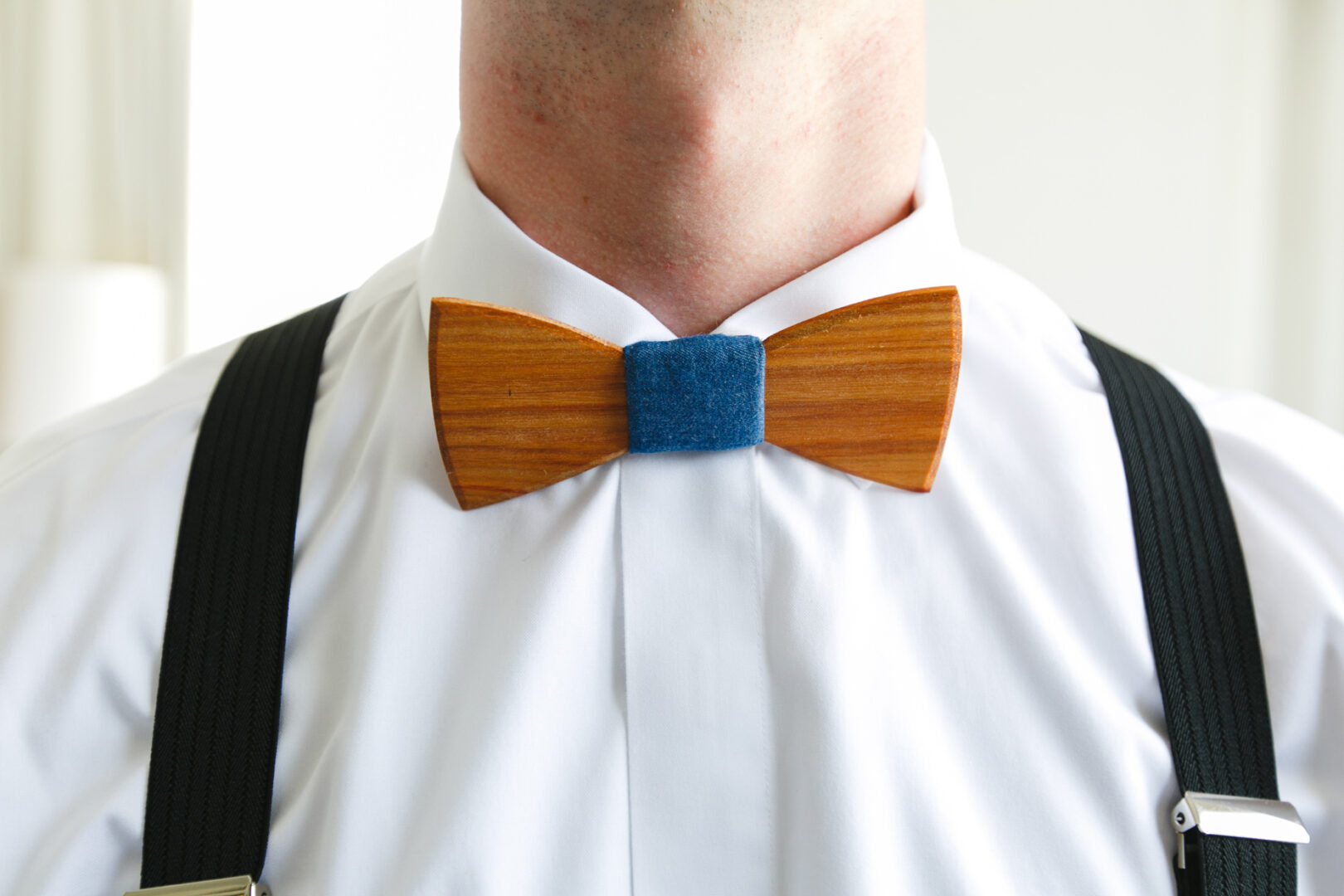 Close-up of a person wearing a white shirt with black suspenders and a wooden bow tie with a blue center, capturing the charm of an elegant Please Touch Museum wedding attire.