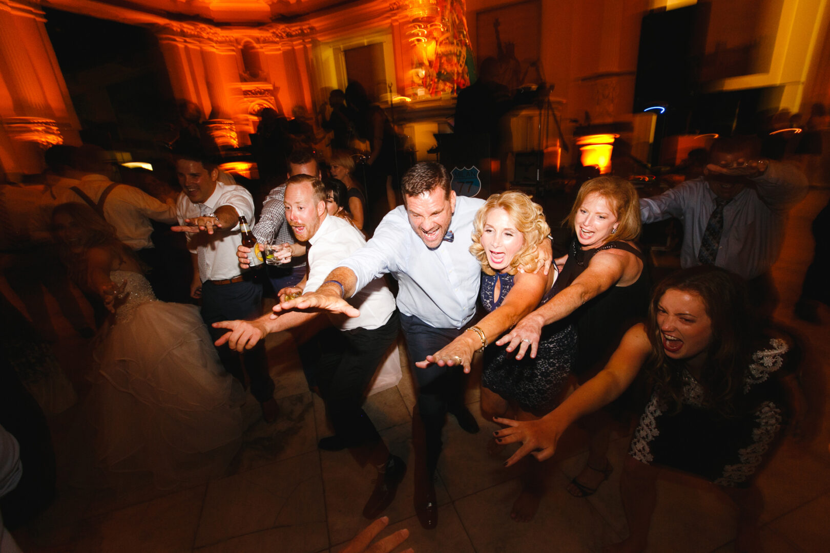 A group of people joyfully reaching forward, smiling and dancing in a warmly lit room, as if celebrating a magical Please Touch Museum wedding.