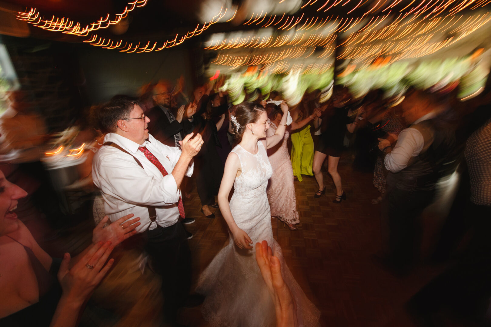 At their enchanting Rockwood Park Carriage House wedding, the bride and groom walk through a cheering crowd on a vibrant dance floor, with blurred lights overhead creating a dynamic effect.