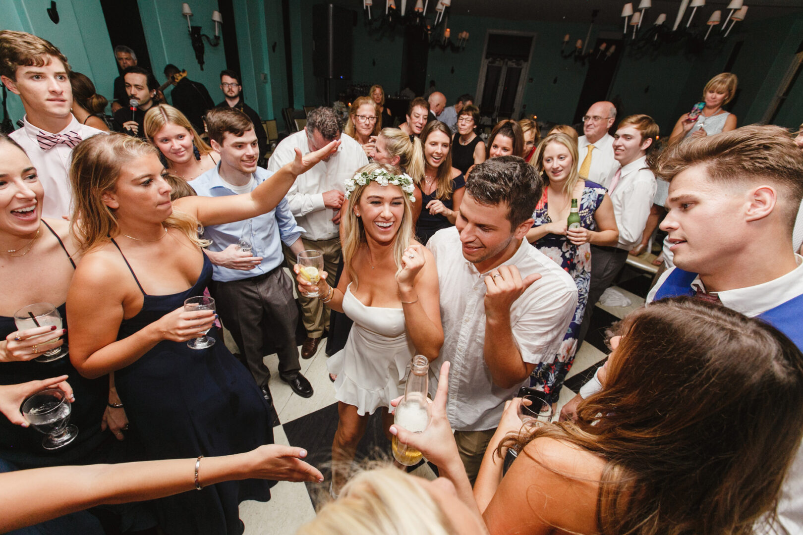 A lively crowd danced and socialized at the party, with a woman wearing a floral crown at the center, celebrating as if it were a Congress Hall Cape May wedding.