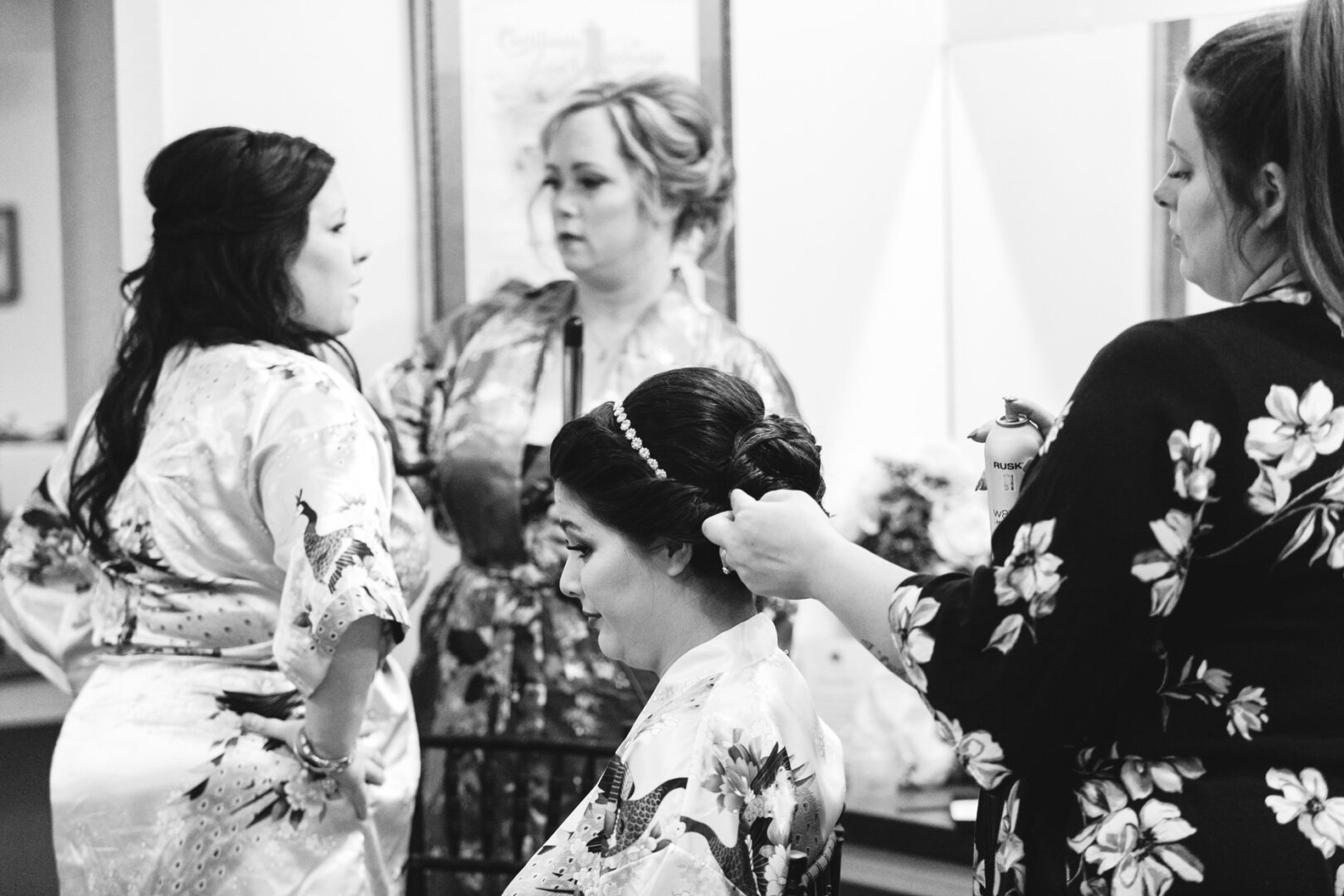 Four women in floral robes are in a room at Brandywine Manor House. One is seated while another styles her hair, perfectly capturing the essence of a wedding morning. The other two are standing, engaged in lively conversation, adding to the joyous atmosphere.