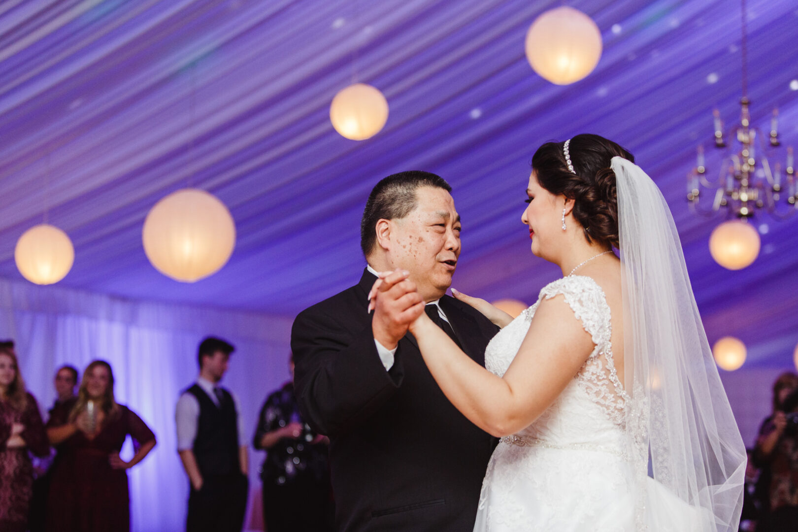 At a charming Brandywine Manor House wedding, the groom and bride gracefully dance together under a tent adorned with magical hanging lights.