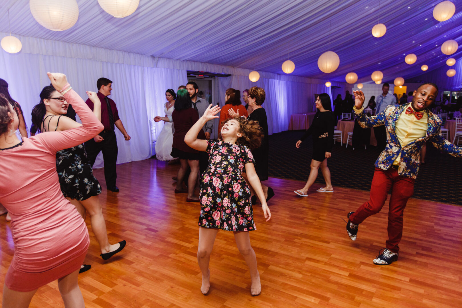 People dancing enthusiastically on a wooden floor at a Brandywine Manor House wedding, surrounded by an event space lit with hanging paper lanterns.