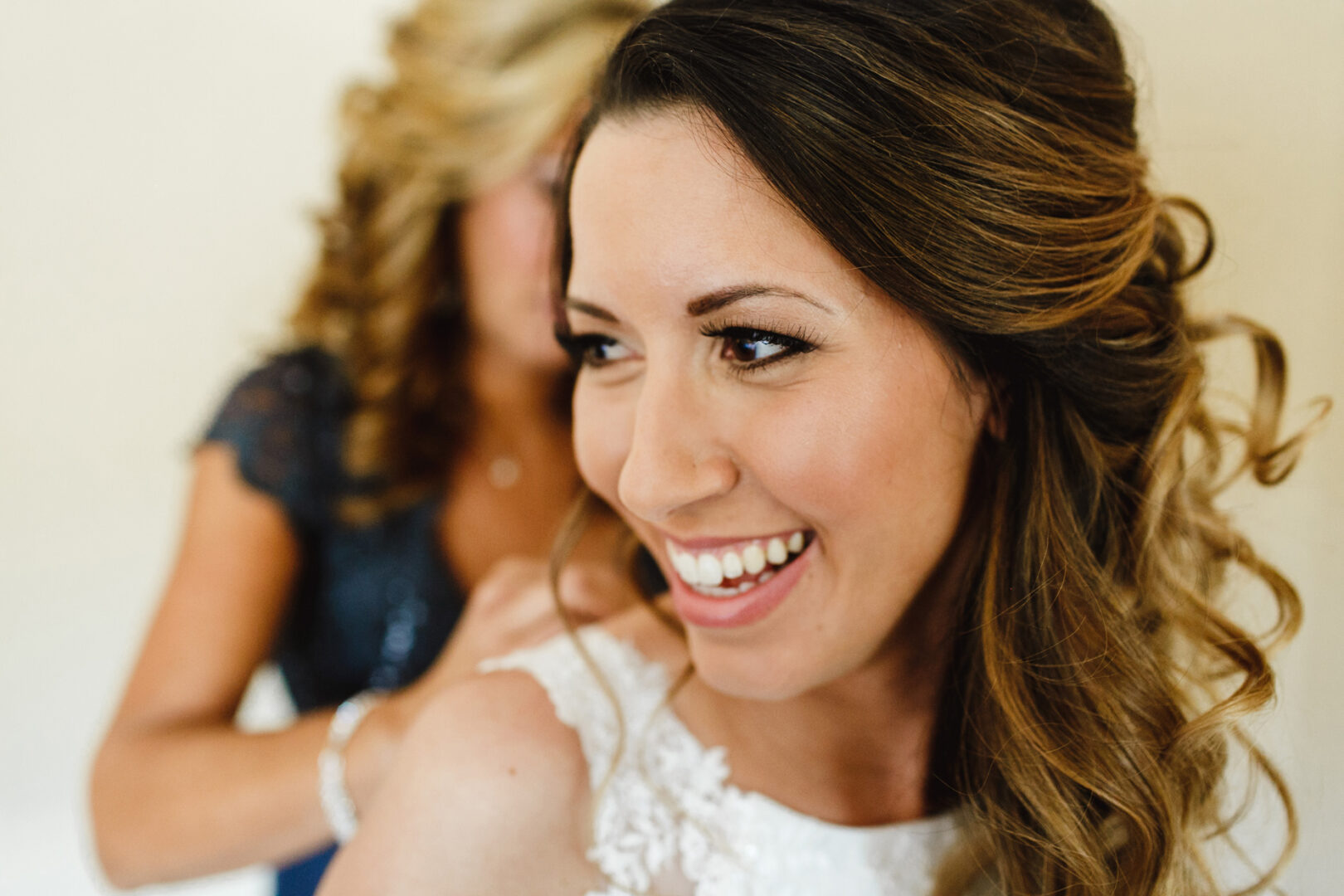 A woman beams with joy as another person helps adjust her dress in the elegant Windsor Ballroom, setting the stage for a perfect wedding day.