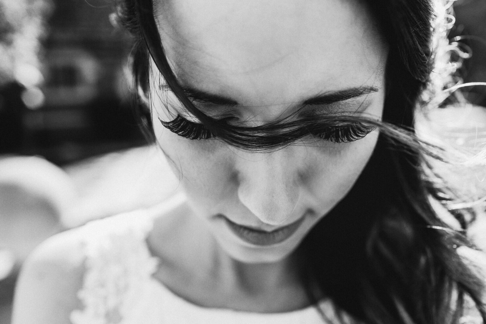 Black and white close-up of a woman looking down. Her hair blows across her face, highlighting long eyelashes, reminiscent of a moment in the Windsor Ballroom on a wedding day.