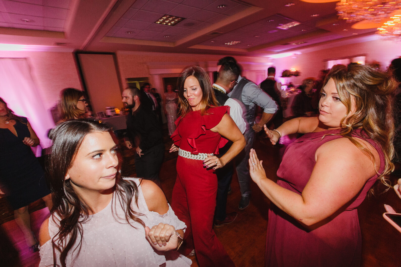 A group of people dances gracefully in the Windsor Ballroom, bathed in soft pink lighting. Some guests, adorned in elegant formal attire, swirl across the floor, creating a magical wedding atmosphere.