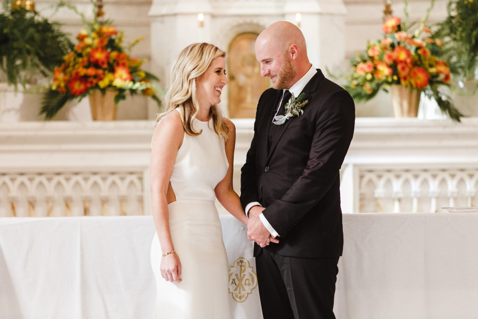 A couple in elegant wedding attire stands smiling in front of an altar adorned with beautiful floral arrangements, capturing the magic of a Congress Hall wedding.