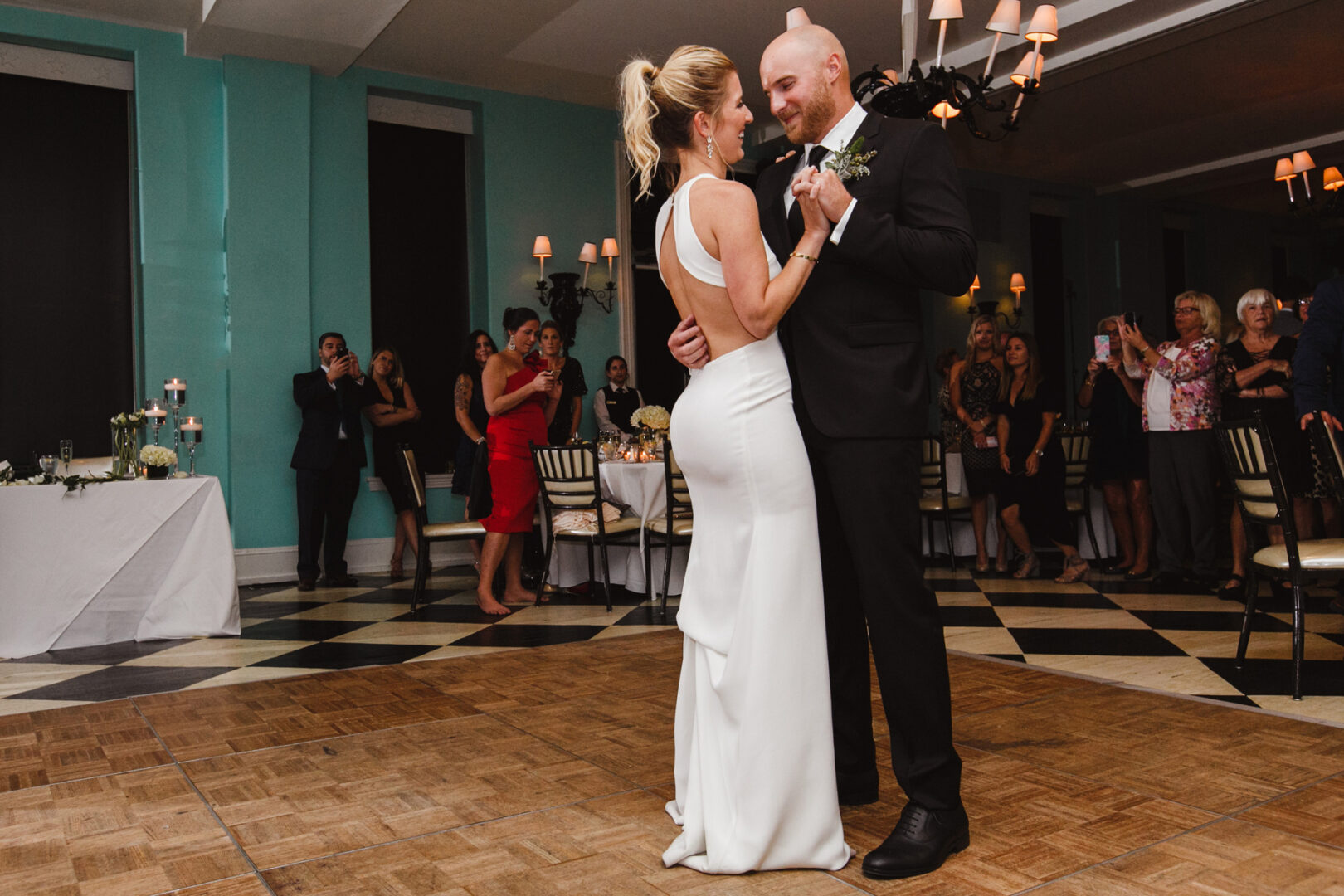 At a Congress Hall wedding, a bride and groom share an enchanting dance on the elegant wooden floor of the reception hall, surrounded by joyous guests.