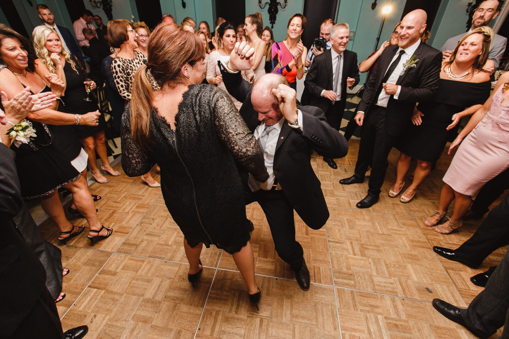 A crowded dance floor at Congress Hall. A man in a suit dances energetically with a woman in a black dress during the wedding celebration, while others watch and smile.