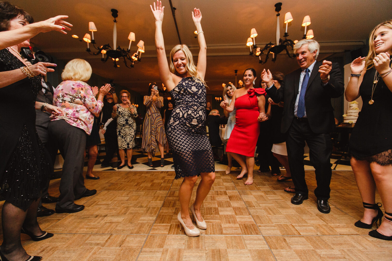 A woman in a blue dress dances with raised arms on the Congress Hall dance floor, surrounded by people clapping and smiling at the wedding celebration.