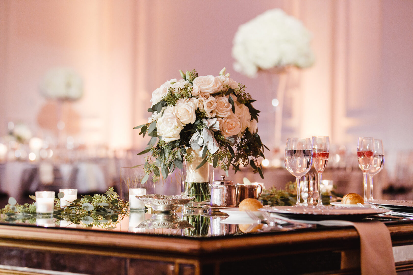 Elegant table setting with a floral centerpiece, wine glasses, candles, and plates on a reflective surface in a warmly lit room, perfect for an intimate downtown club wedding.