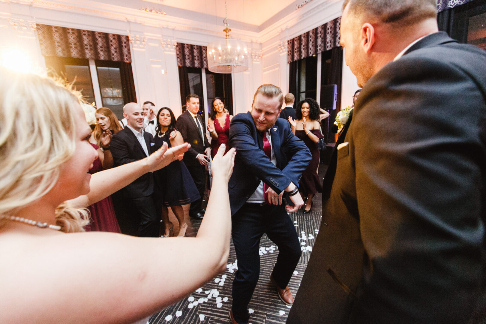 A man energetically dances in the center of a downtown club party while people stand around watching and smiling.