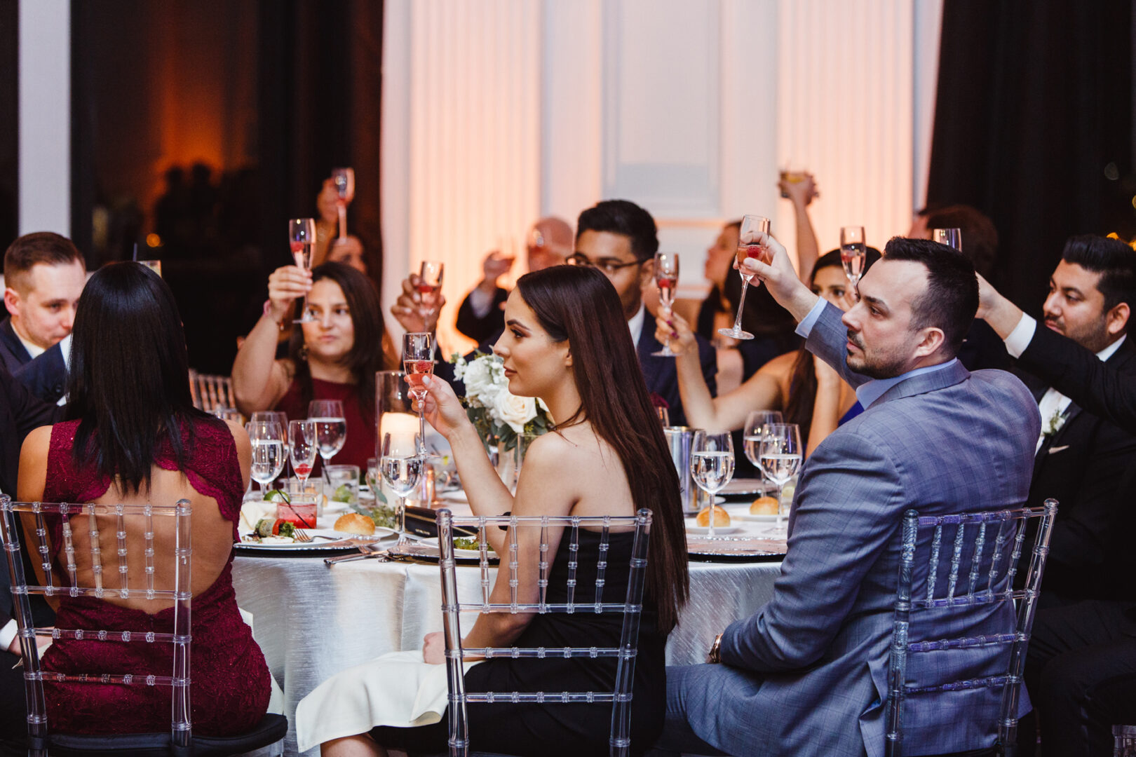 A group of people seated around a table at the Downtown Club raise their glasses in a toast during an indoor formal event.
