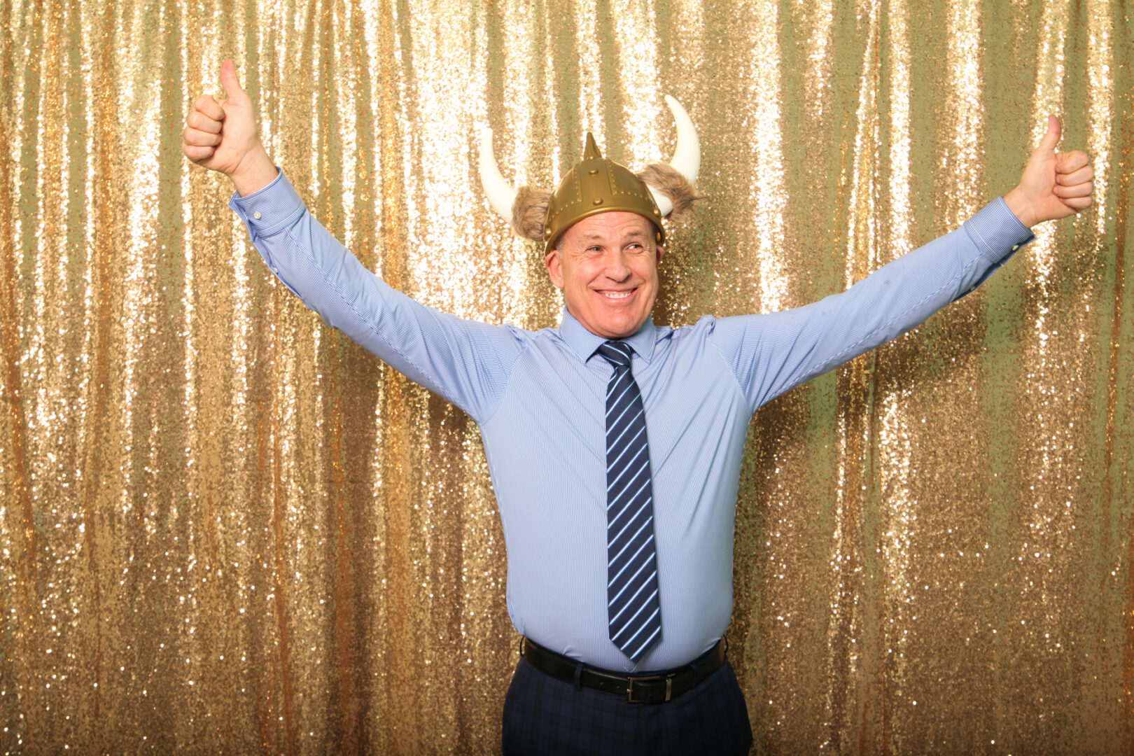 A man wearing a Viking helmet and a blue shirt gives two thumbs up in front of a gold sequin backdrop, adding an extra layer of fun to this memorable Cape May Photo Booth moment.