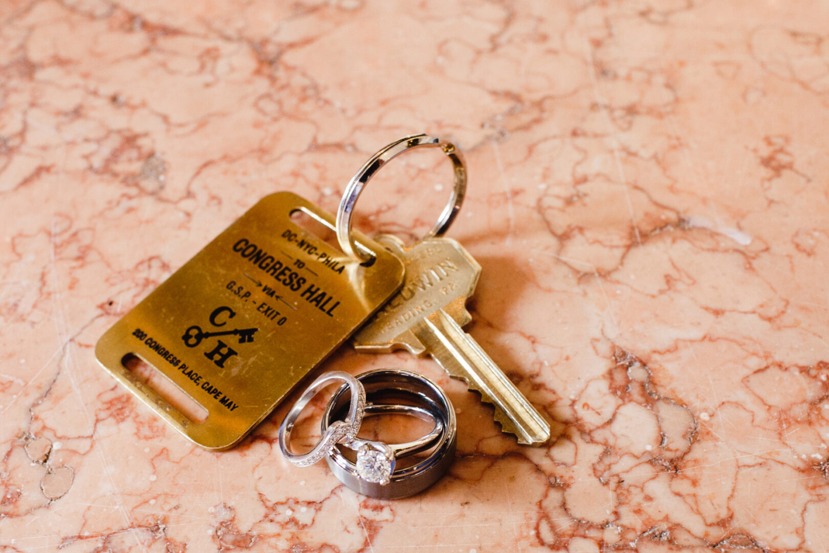 A charming key with a Congress Hall tag and two rings rests elegantly on a marble surface, hinting at the timeless beauty of a Cape May wedding.