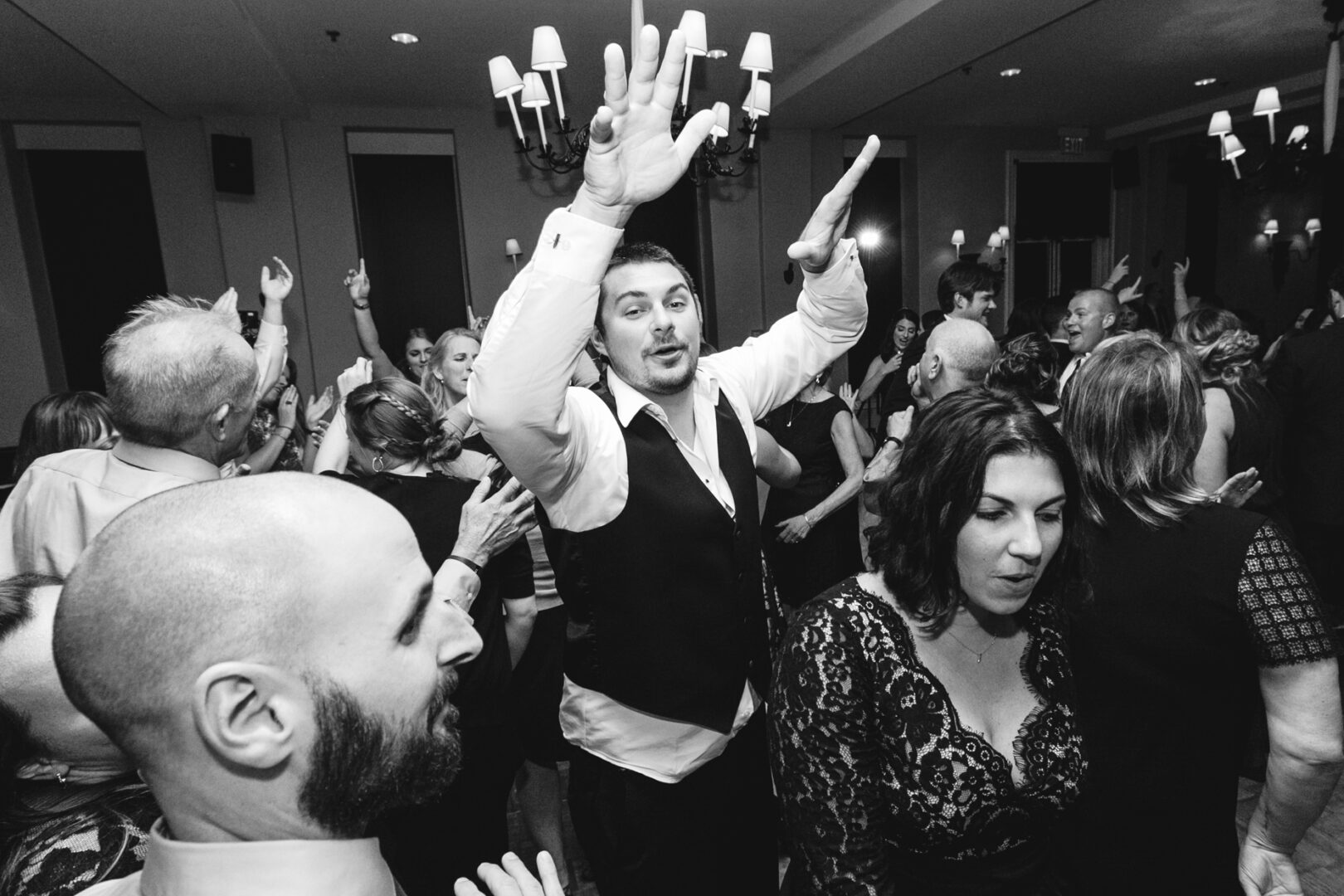 A lively crowd dances at a Cape May wedding, with a man in a vest raising his hands and others moving energetically around him.