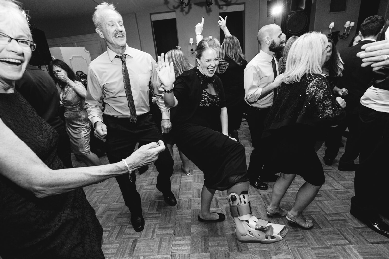 At a festive Cape May wedding, guests dance energetically, the joyful atmosphere unaffected by one woman stylishly swaying in her medical boot as she joins in the celebration.