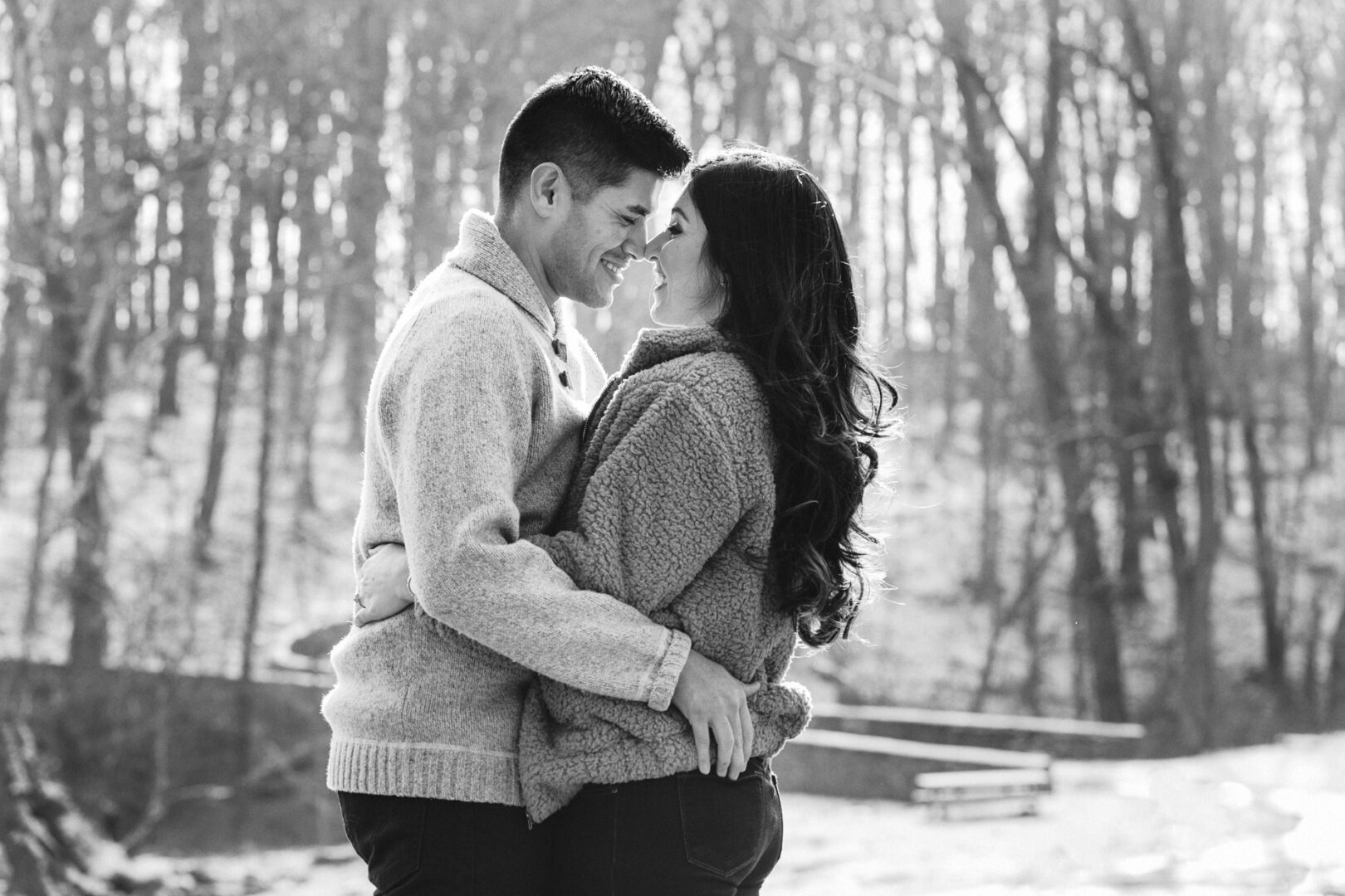 In a magical New Hope engagement session, a couple stands closely in a snowy wooded area, gazing at each other affectionately with bare trees in the background.