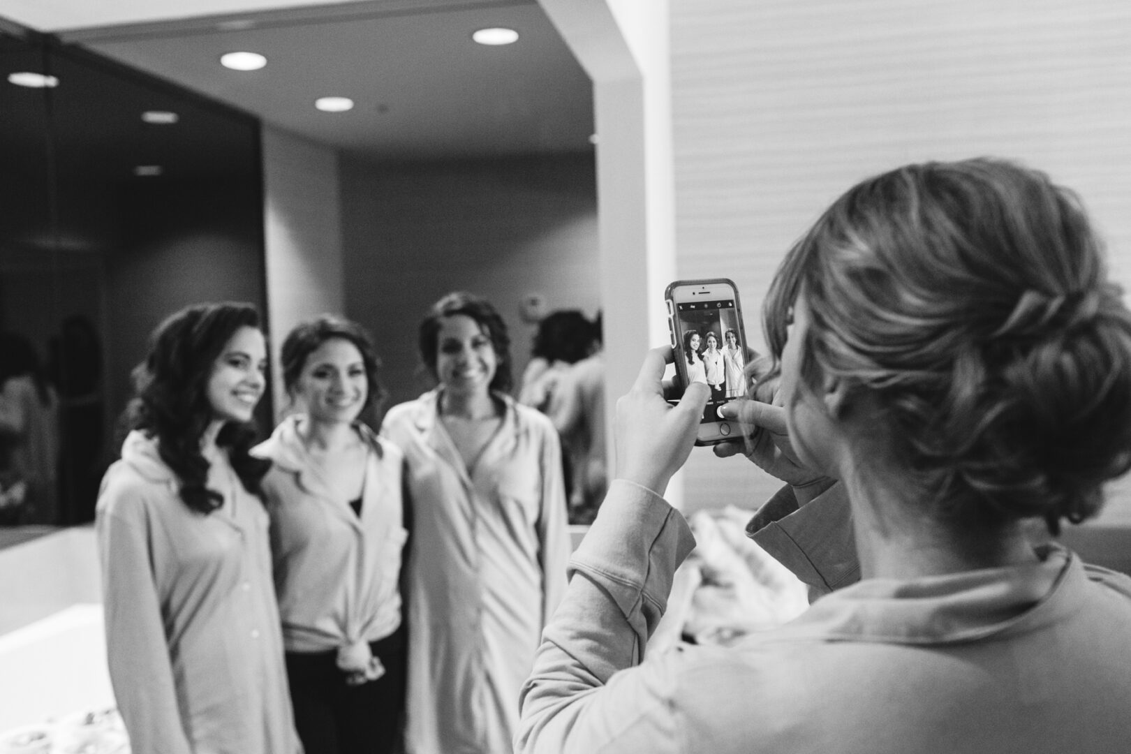 Three women pose elegantly for a mirror photo, capturing the joyful essence of the Palace at Somerset Park wedding, as another person snaps the picture with a smartphone. The indoor setting adds an intimate touch to this memorable moment.