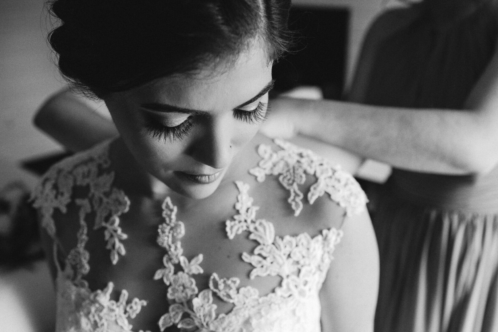 Bride in lace dress getting gown adjustments at the elegant Palace at Somerset Park, captured in black and white, focusing on intricate details and expression.
