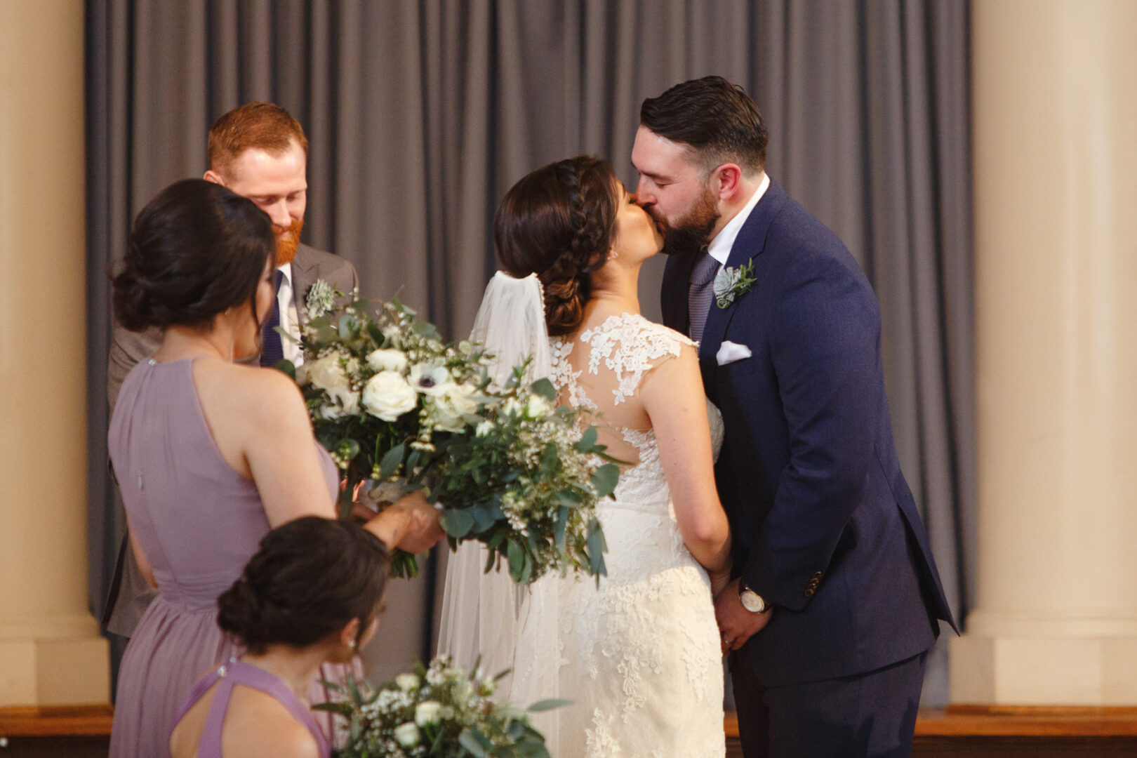 A bride and groom share a kiss during their Palace at Somerset Park wedding ceremony, with two bridesmaids holding flower bouquets nearby.