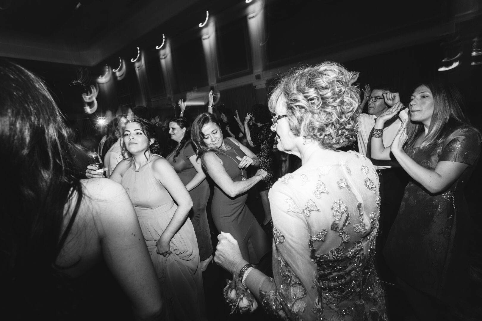 In the elegant setting of the Palace at Somerset Park, a group of people dance energetically, some with drinks in hand while others raise their arms high. The indoor celebration buzzes with a lively and jubilant spirit, making it a night to remember.