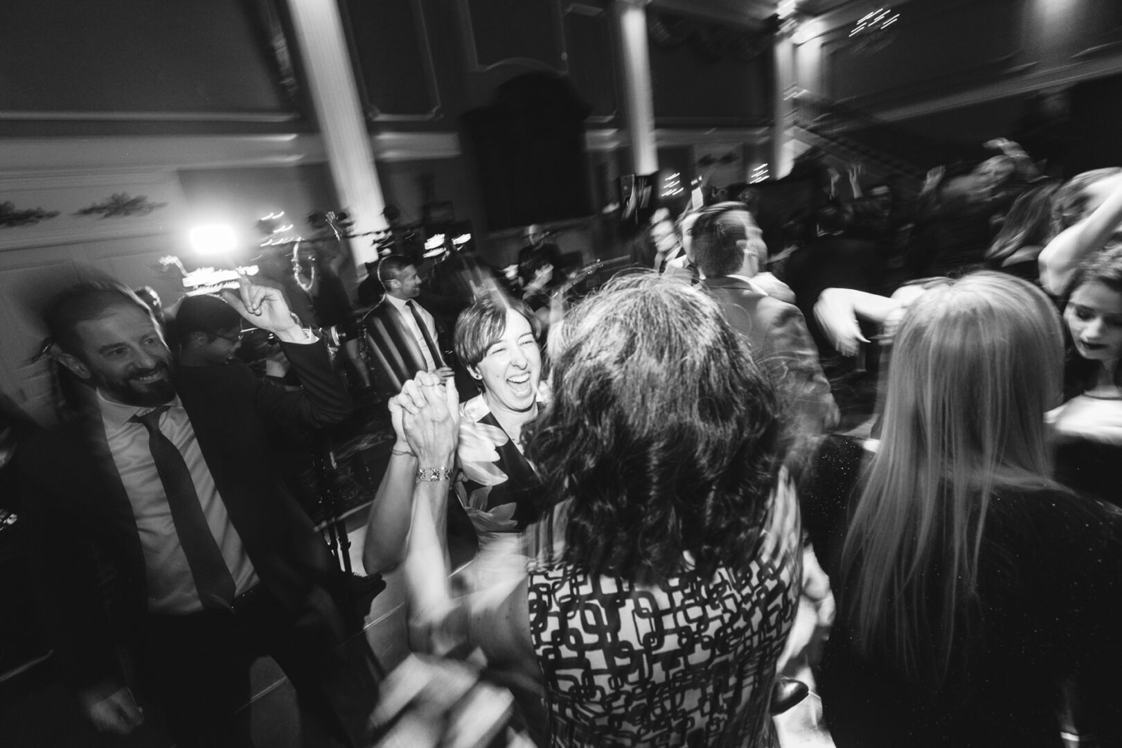 A black and white image captures guests dancing energetically at a Palace at Somerset Park wedding, their lively expressions and the blurred motion illustrating the room's vibrant energy.