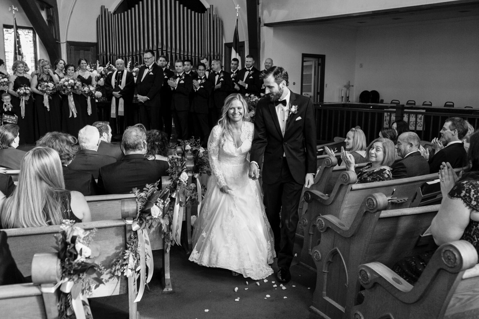 A bride and groom walk down the aisle together in a church filled with guests, their smiles as bright as a sunny day at Willow Creek Winery. The wedding party stands proudly in the background, completing the perfect scene.