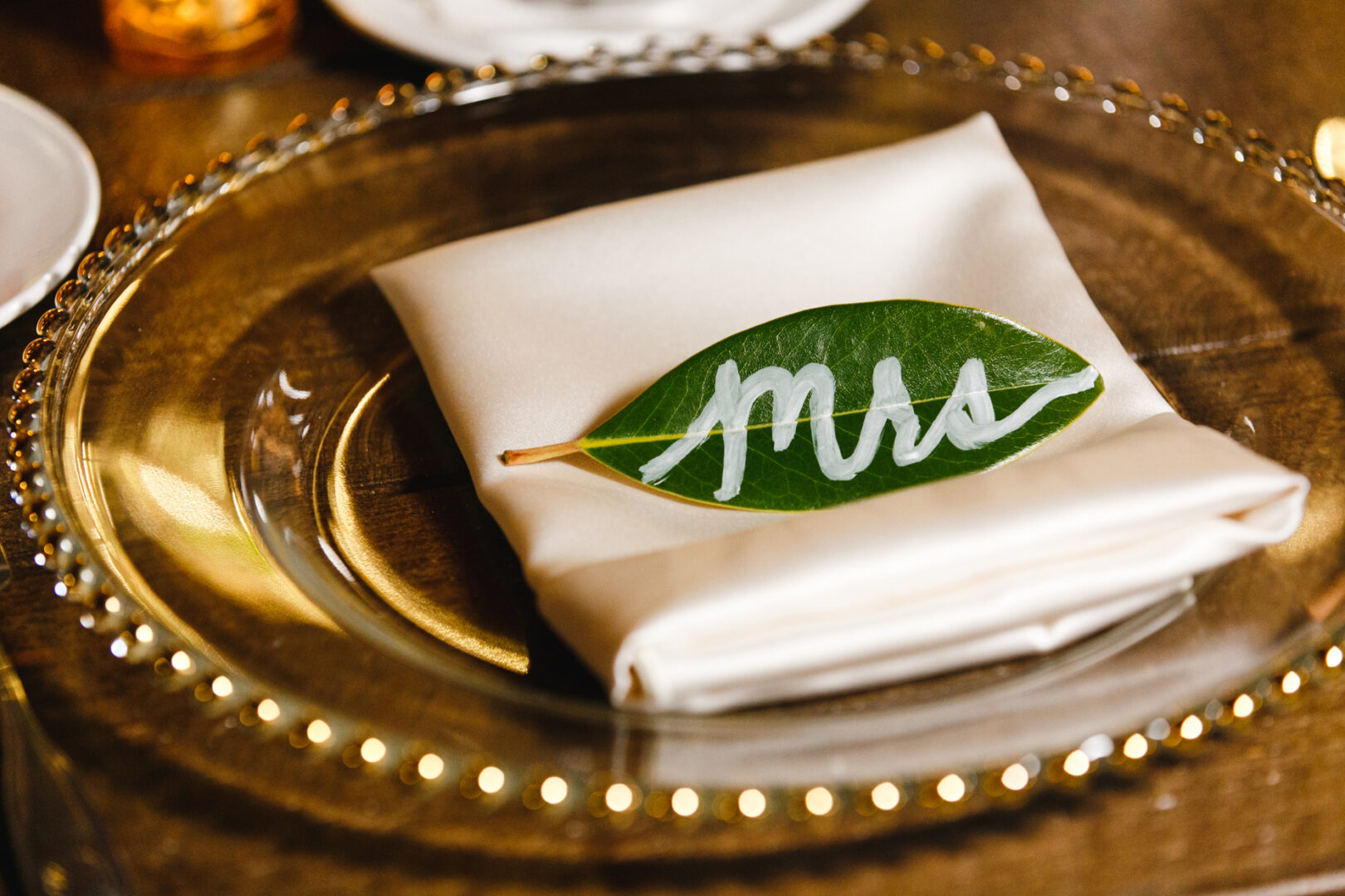 A leaf with "Mrs" written on it sits gracefully atop a folded white napkin on a clear beaded glass plate, capturing the elegance of a Willow Creek Winery setting.