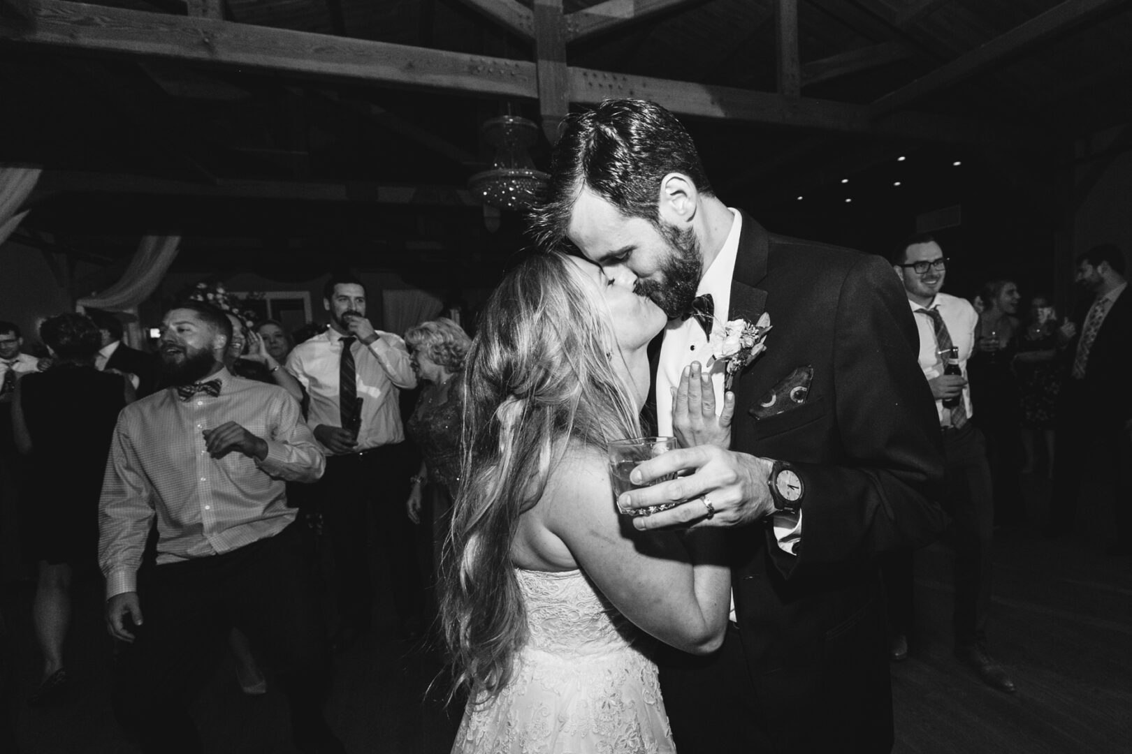 At Willow Creek Winery, a couple in formal attire shares a tender kiss on the dance floor at a wedding reception, surrounded by delighted guests.