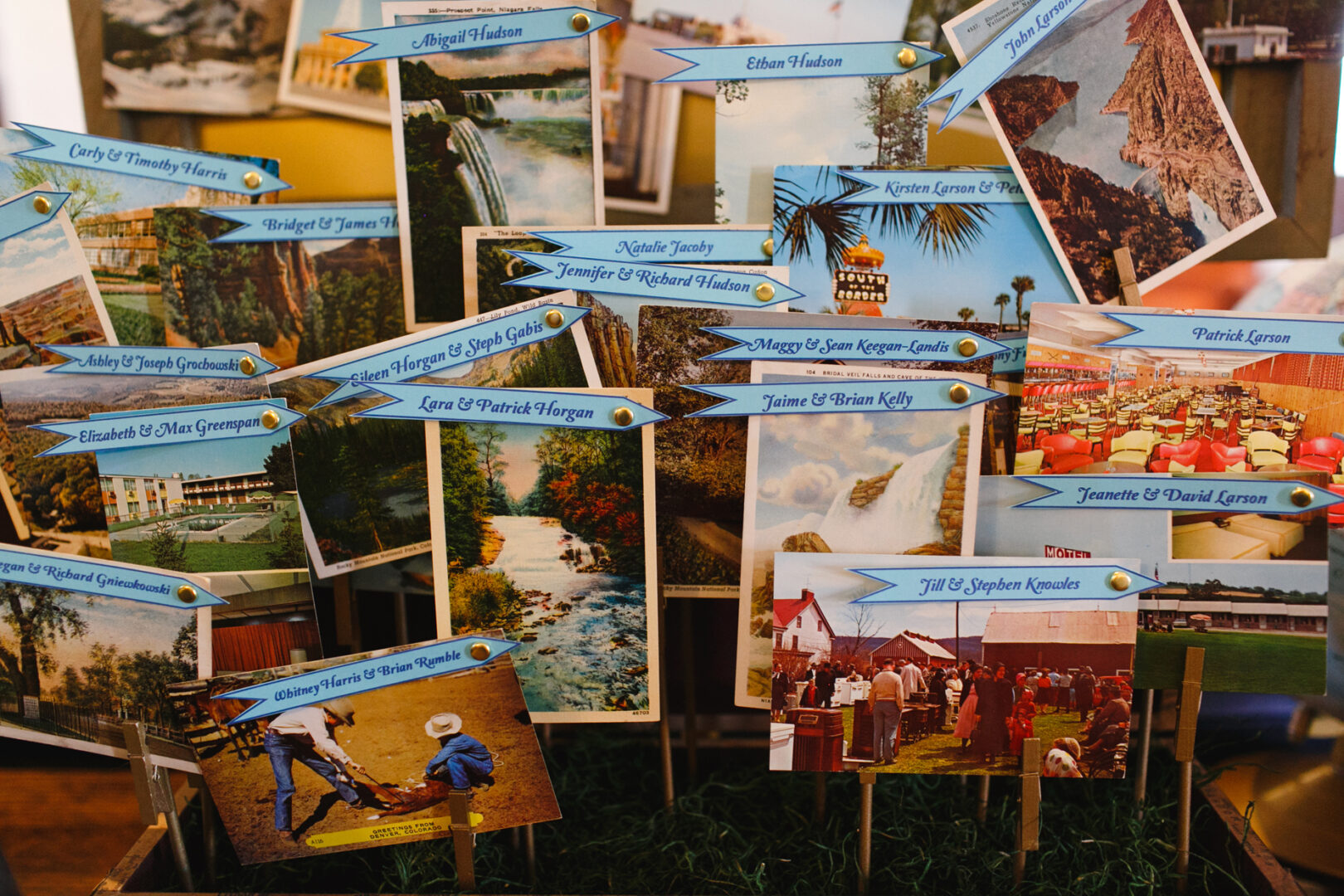A collection of postcards and photos pinned on a display board, each labeled with names and event details like the enchanting Baldwin School wedding, all adorned with blue banners.