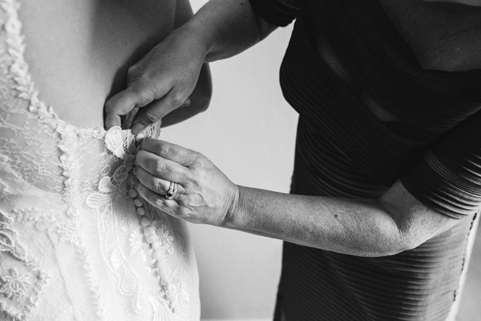 At a Baldwin School wedding, a person delicately fastens buttons on the back of a lace wedding dress.