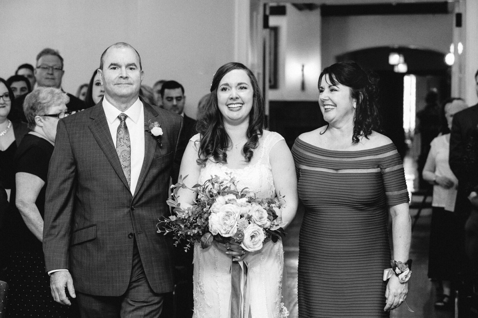 At a charming Baldwin School wedding, a bride gracefully walks down the aisle, bouquet in hand, flanked by her closest companions.