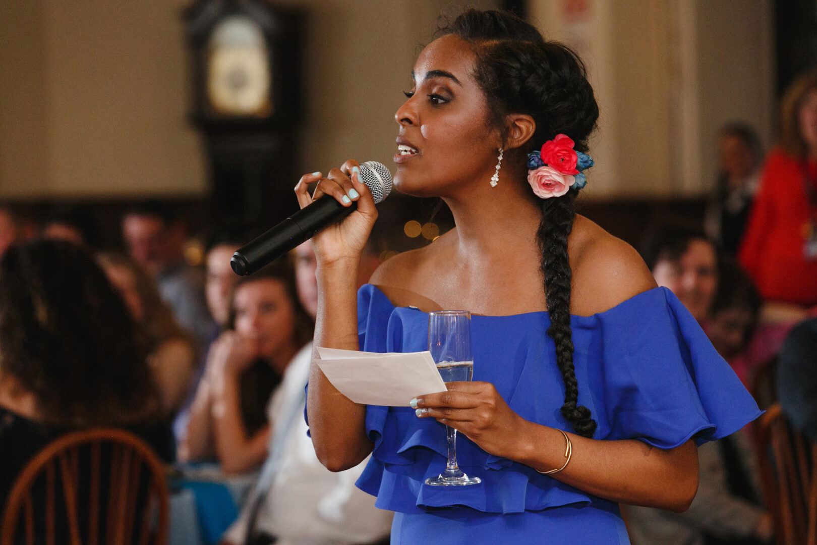 At a Baldwin School event, the woman in a blue dress captivated the seated audience with her poised delivery, microphone and speech notes in hand, as if orchestrating a beautiful wedding ceremony.