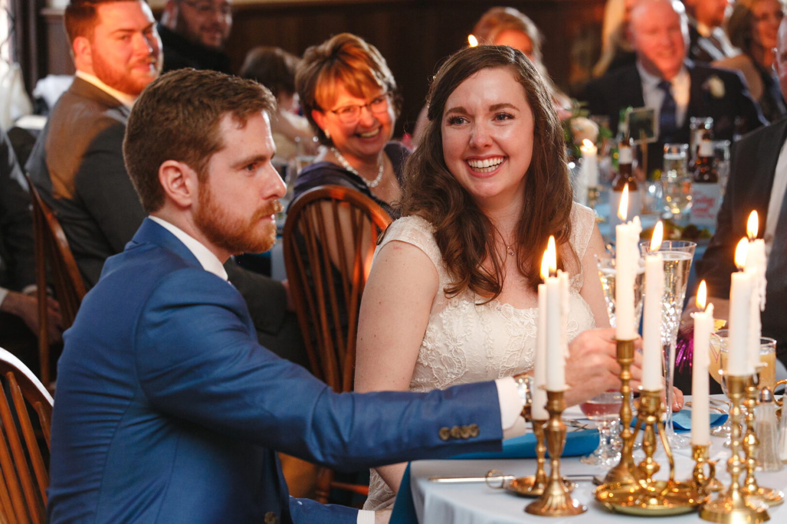 At a beautifully adorned Baldwin School wedding, a bride and groom share an intimate moment at their candlelit table, surrounded by the warm smiles of cherished guests.