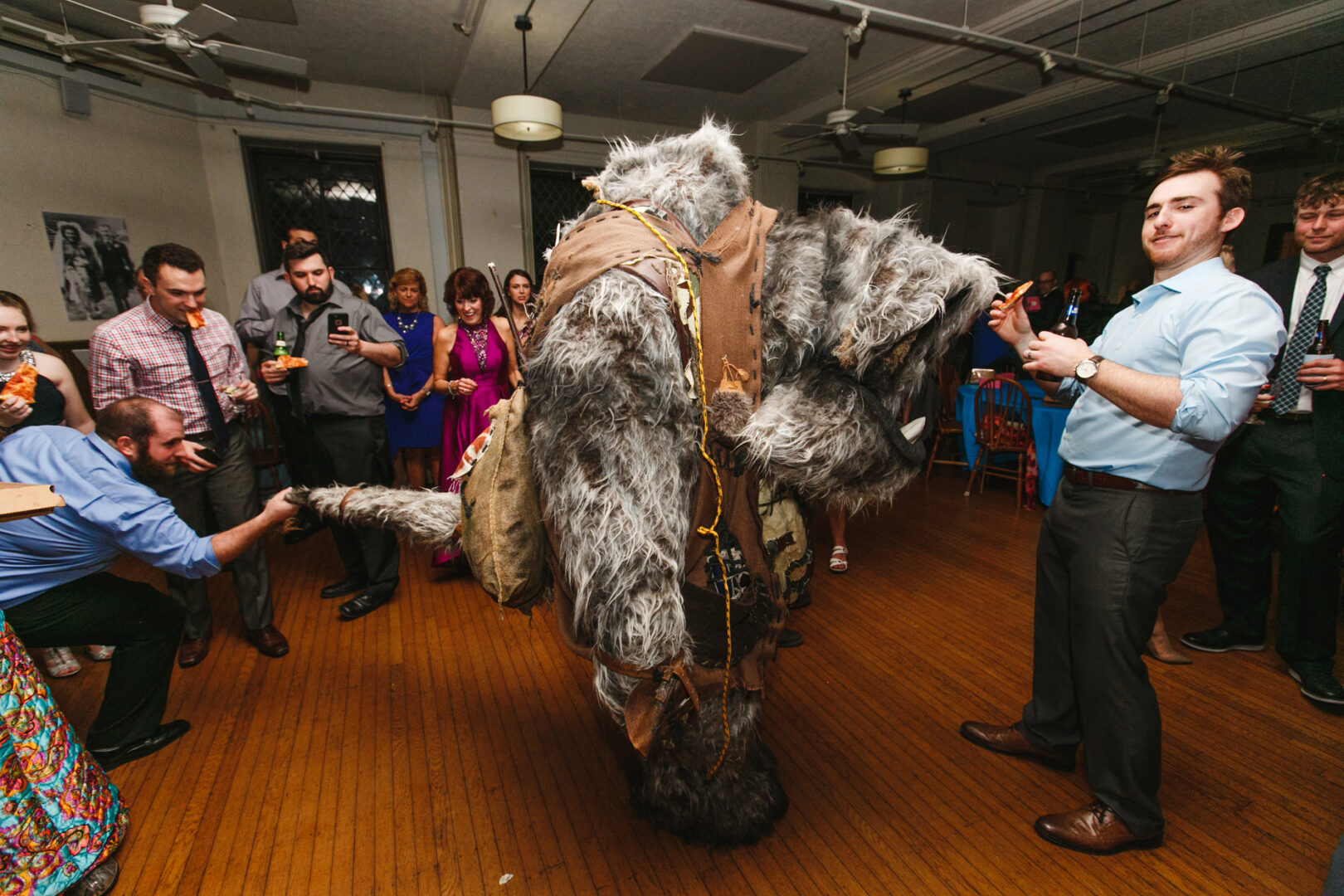 At a Baldwin School wedding, a person in a large, furry costume resembling a mythical creature entertains the elegantly dressed guests at the indoor event.
