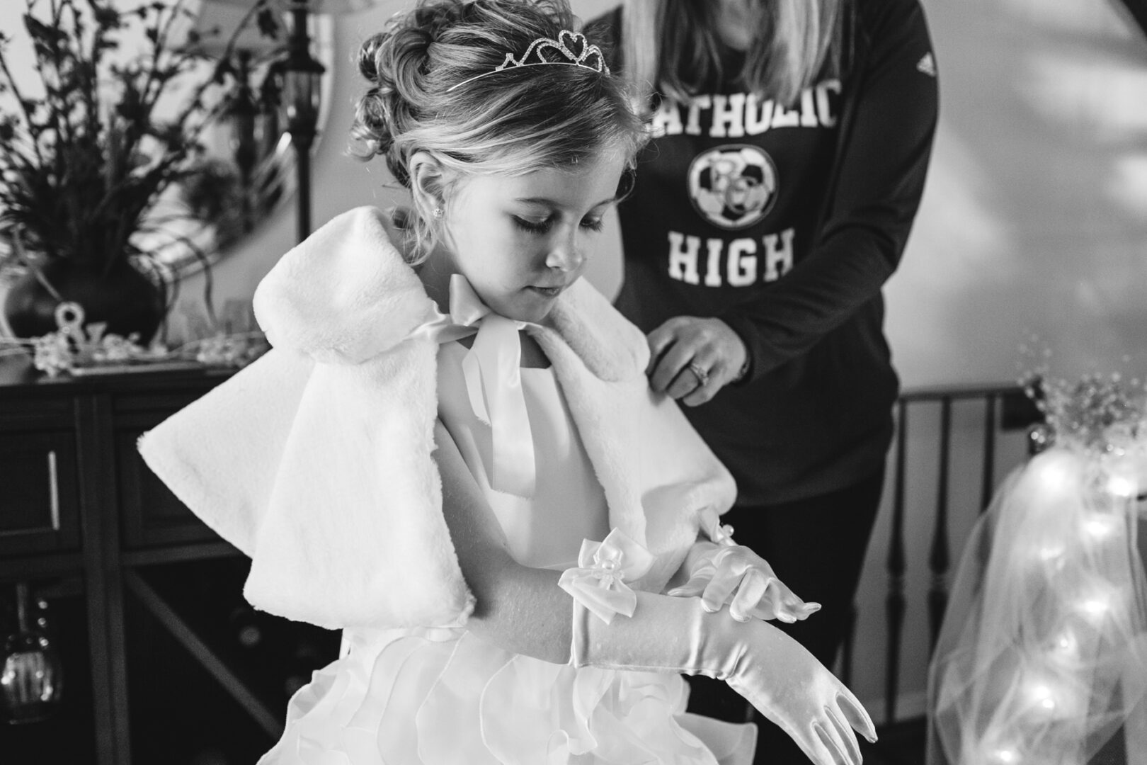 A young girl in a formal dress and tiara is being helped with her gloves by an adult, adding a touch of elegance to the enchanting atmosphere of a Crystal Tea Room wedding.