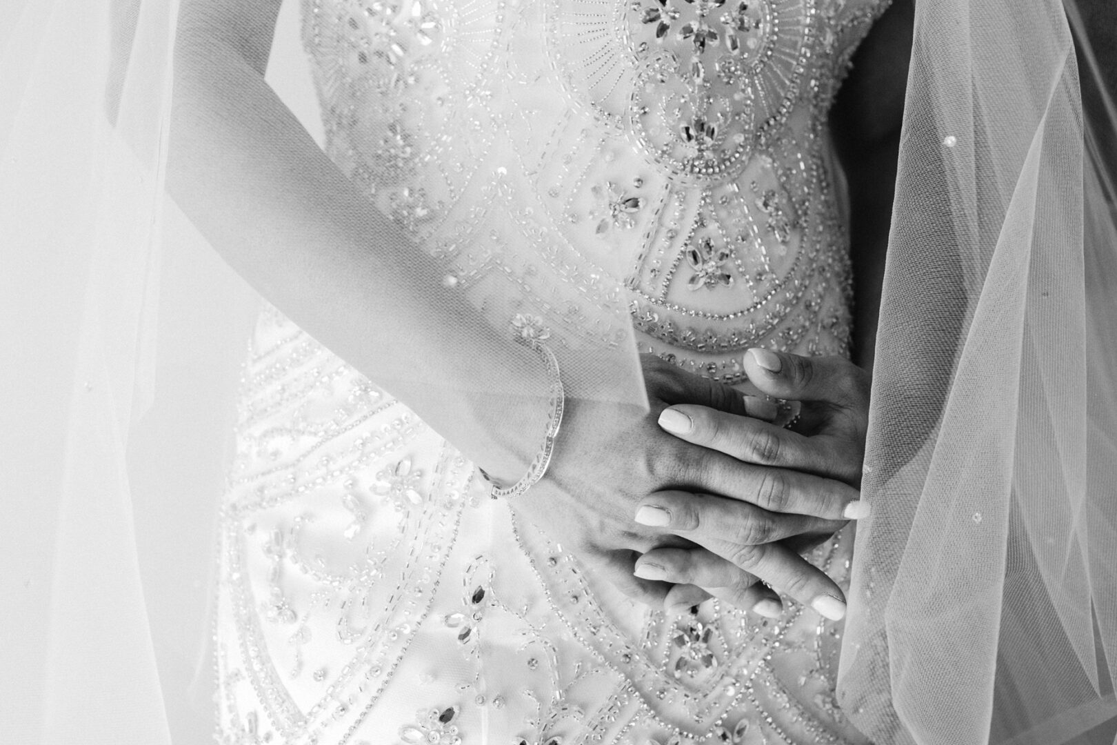 Bride's hands rest on her ornate, beaded wedding dress at the Crystal Tea Room wedding, with a veil partially in view.