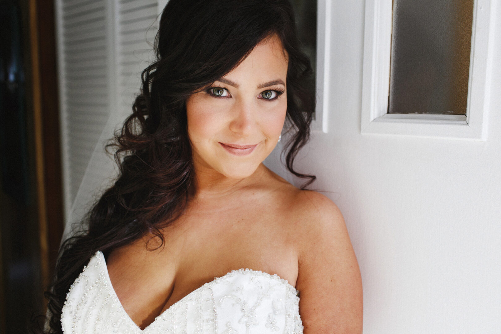 A woman with long dark hair in a strapless white dress stands indoors at the Crystal Tea Room wedding, smiling slightly at the camera.