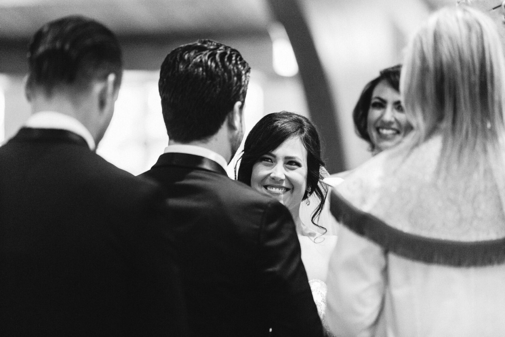 In a timeless black and white photo of a Crystal Tea Room wedding, the bride beams at her groom amidst a sea of guests, as the officiant gracefully conducts the ceremony.
