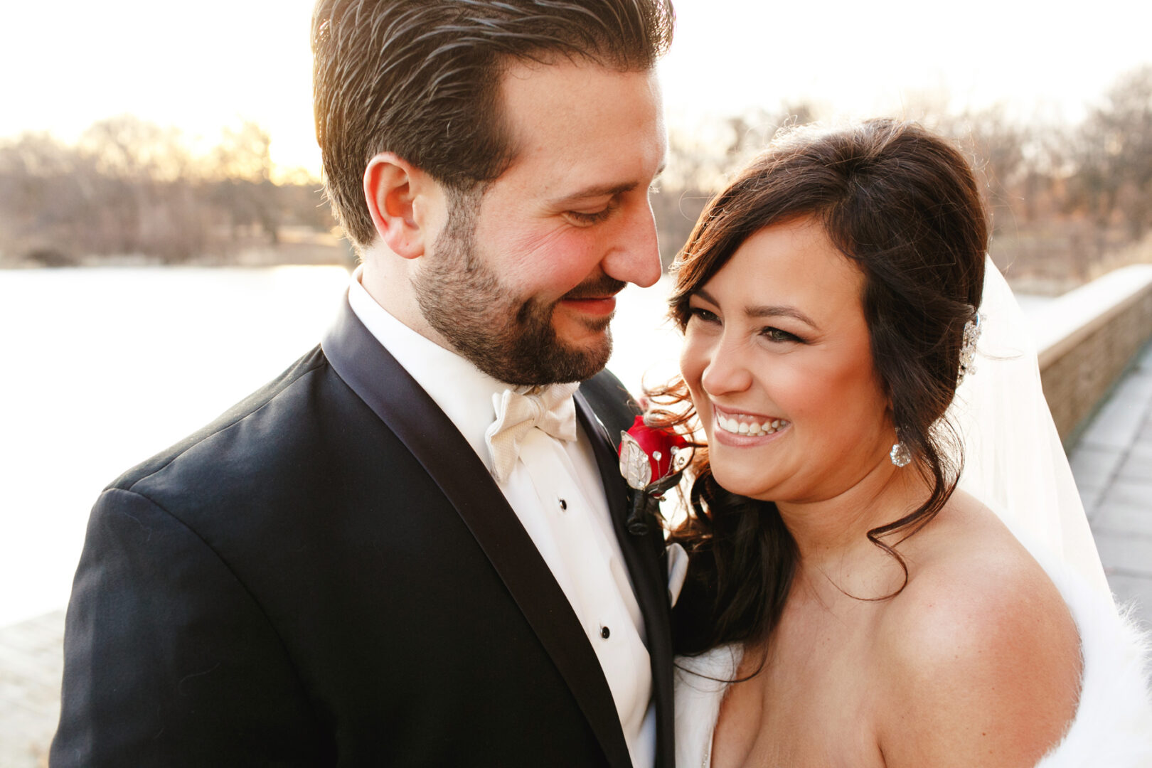 The bride and groom, beaming with joy, stand amidst the natural beauty of trees and a shimmering body of water, reminiscent of a Crystal Tea Room wedding.
