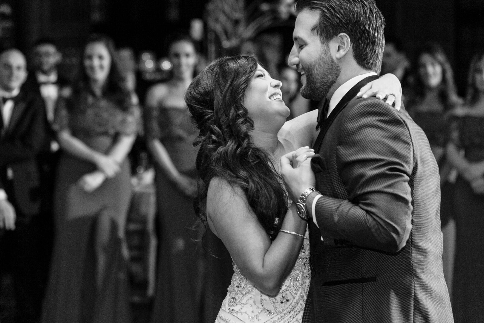 At a Crystal Tea Room wedding, a couple dances closely in front of a group of smiling, formally dressed guests.