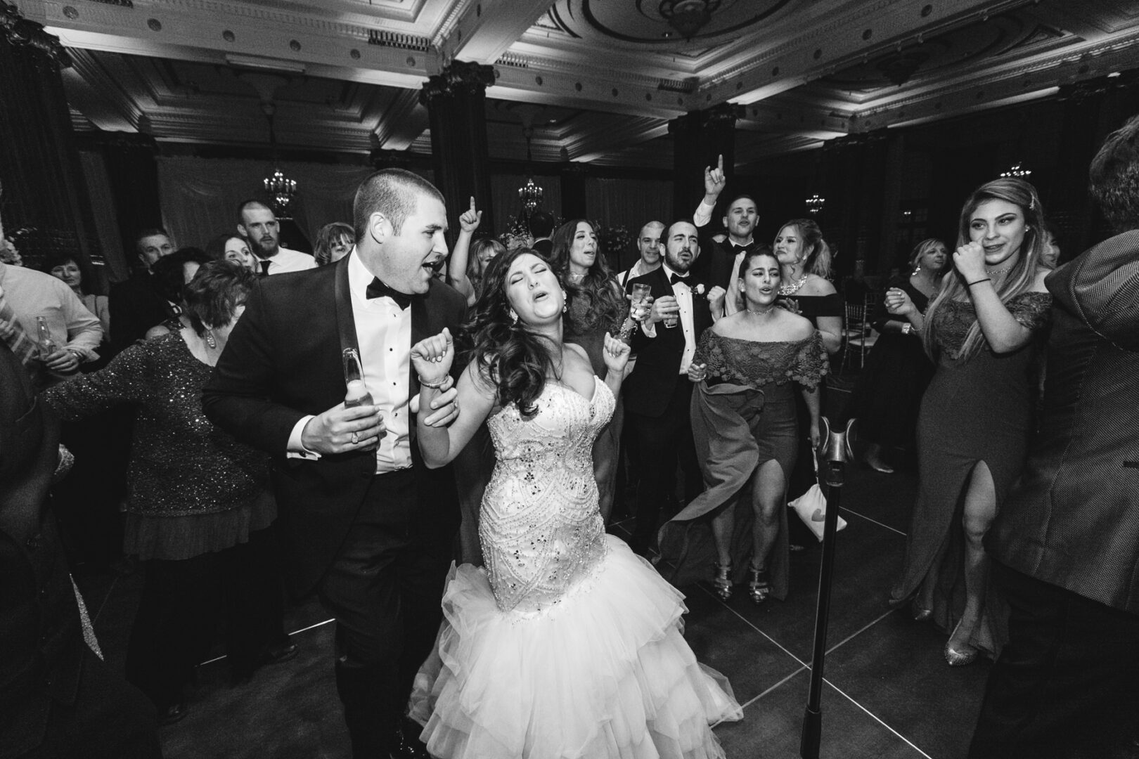 At the Crystal Tea Room wedding, a bride and groom sang and danced enthusiastically on the crowded dance floor, their joy lighting up the elegant venue.