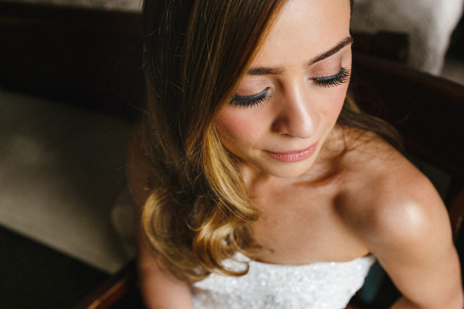 With wavy hair cascading and long eyelashes fluttering, the bride gazes downward in her strapless white dress, exuding timeless elegance at the Michener Art Museum wedding.