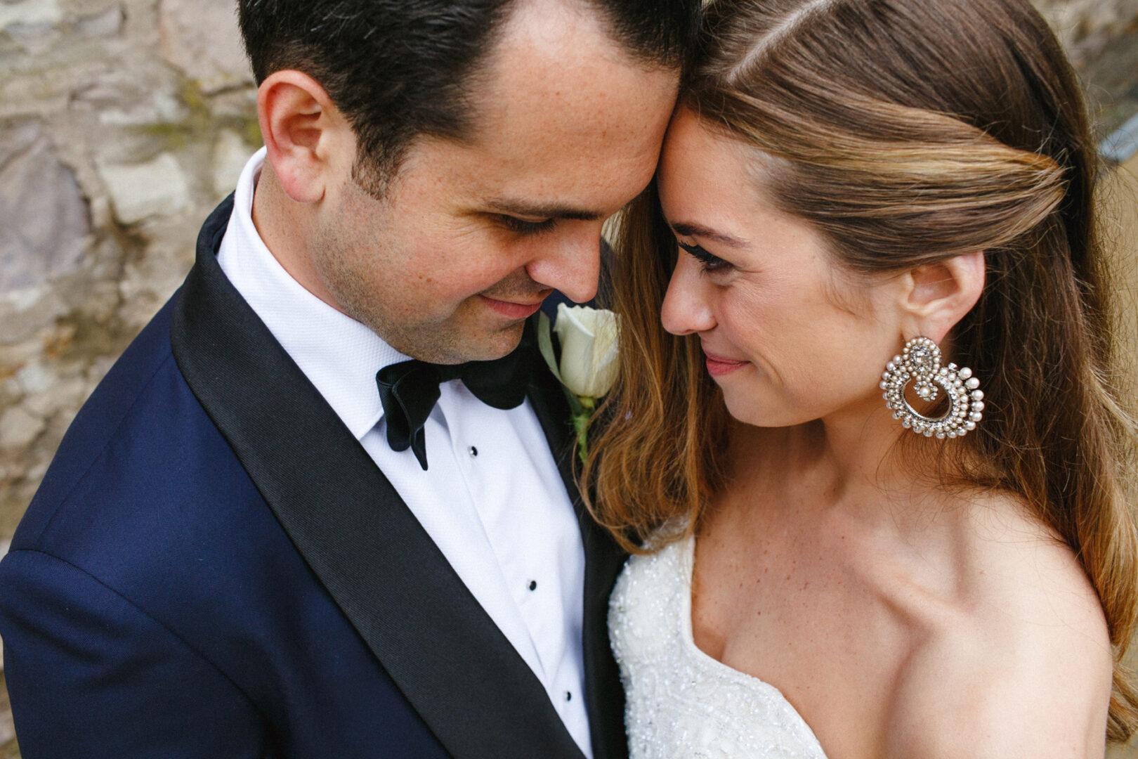 At the Michener Art Museum wedding, a couple dressed in formal attire shares an intimate moment, smiling and touching foreheads. The woman wears large, decorative earrings.