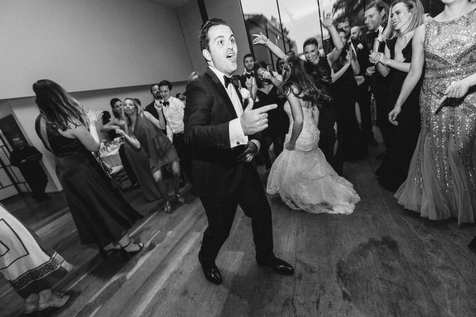 At the Michener Art Museum wedding, a man in a suit energetically gestures while dancing at an indoor event, surrounded by people in formal attire.